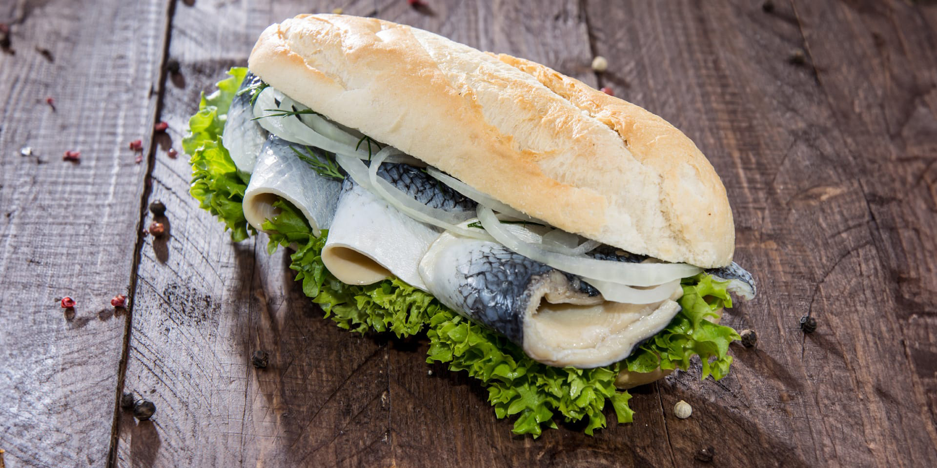 Ein Fischbrötchen mit Hering, Salat und Zwiebeln.