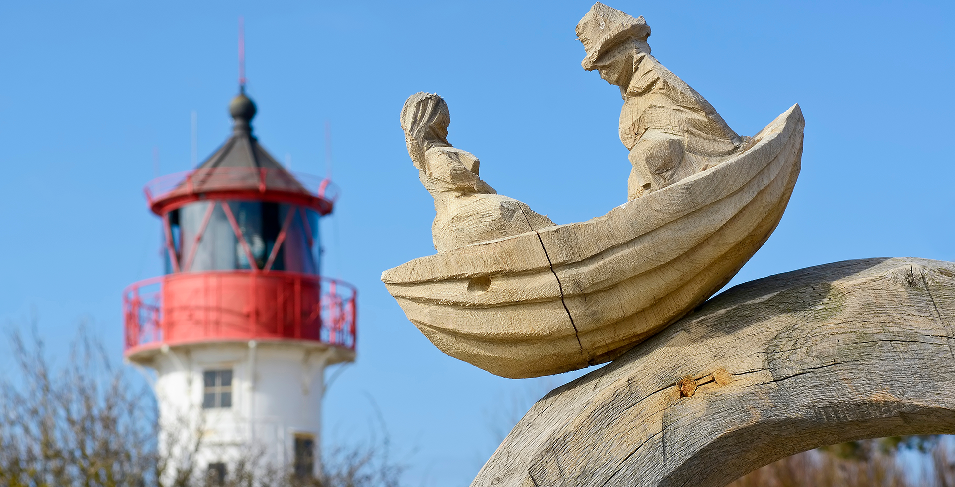 Eine schöne Schnitzerei aus Holz steht vor einem charmanten Leuchtturm auf Rügen. © Adobe Stock, lunaluna