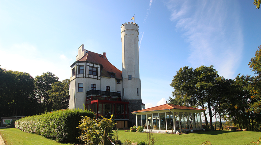 Die historischen Gemäuer des Schlosses Ranzow auf Rügen erstrahlen in Sonnenlicht vor dem Golfplatz. © Adobe Stock, Thomas Kröning